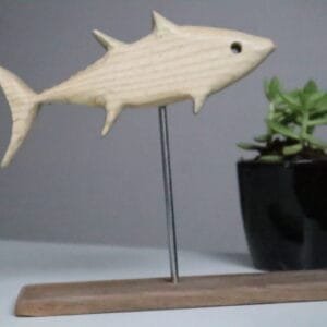 Minimalist white ash wood fish sculpture mounted on stainless steel rod with wooden base, accompanied by a small succulent pot in a modern decor setting. Hand-carved eco-friendly wooden fish figurine displayed on tabletop with indoor plant, ideal for rustic and nature-themed interior styling. Artisan-crafted fish sculpture made of premium white ash wood, designed with clean lines and earthy accents for shelf or desk decor.